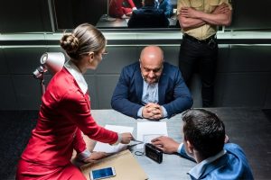 Man in blue suit being questioned by make and female detectives; when accused of a crime, you're initial reaction is important.